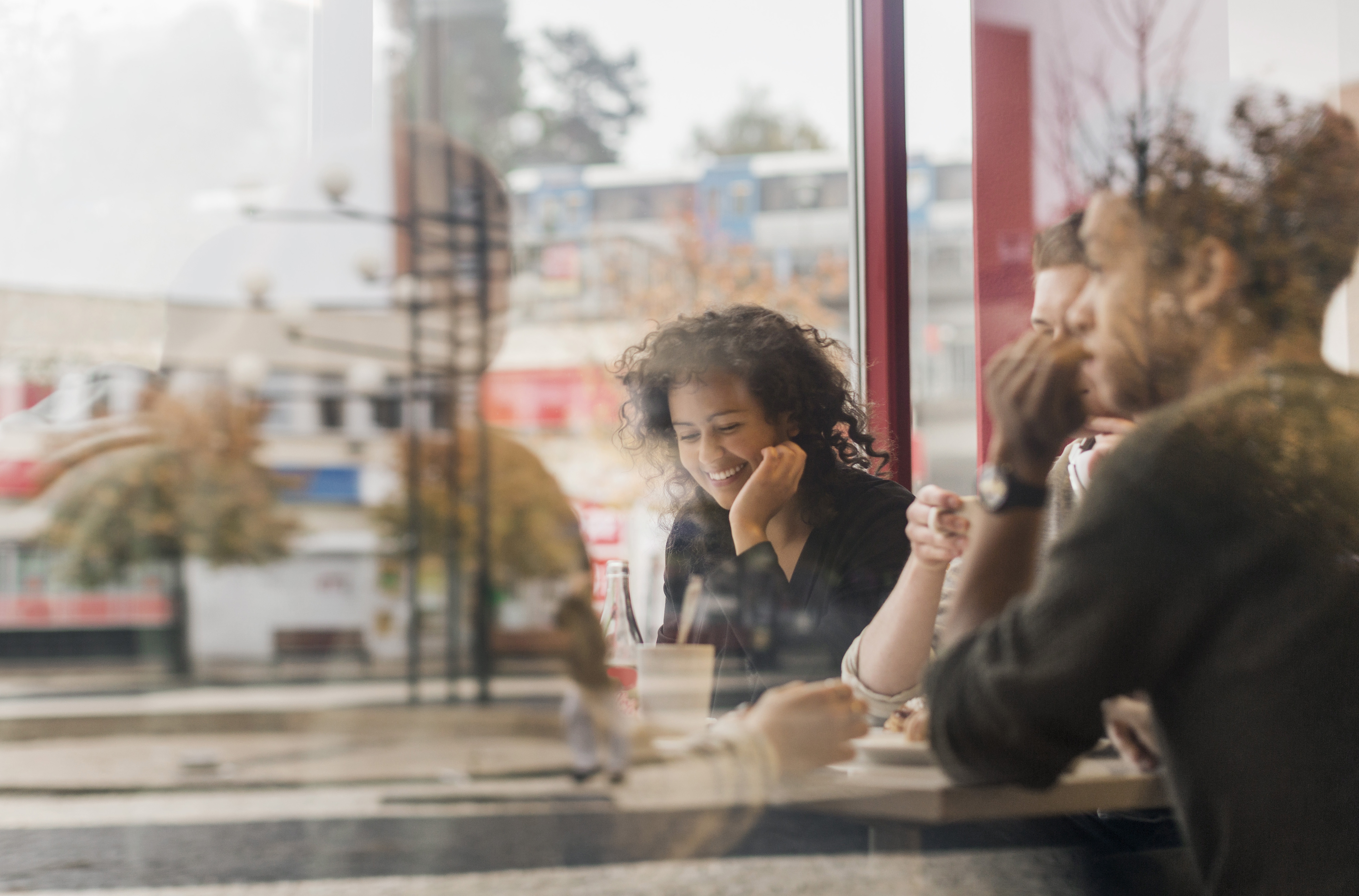 Ung glad kvinna sitter på kafé, genom fönster