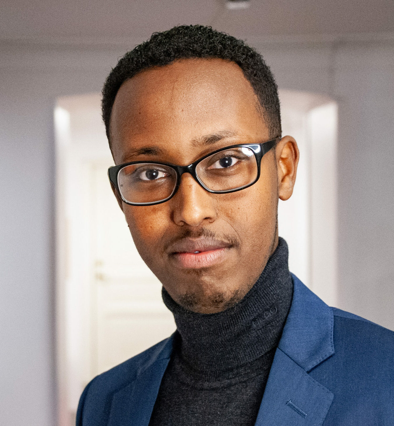 Ahmed tittar in i kameran, han har glasögon, blå kavaj och en röd vänsterpartipin på slaget