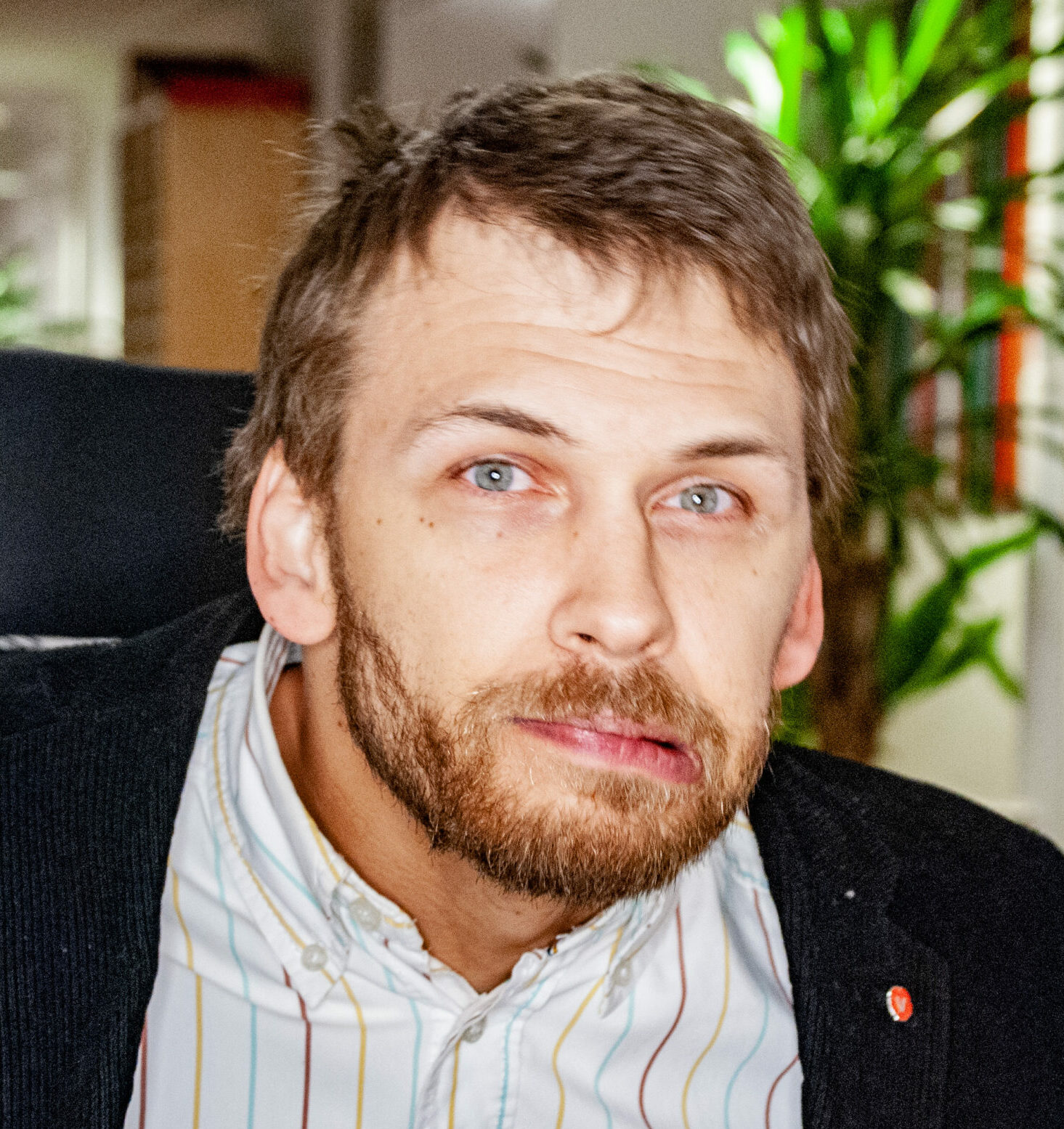 Björn tittar in i kameran, han har randig skjorta och svart kavaj med vänsterpin på slaget.