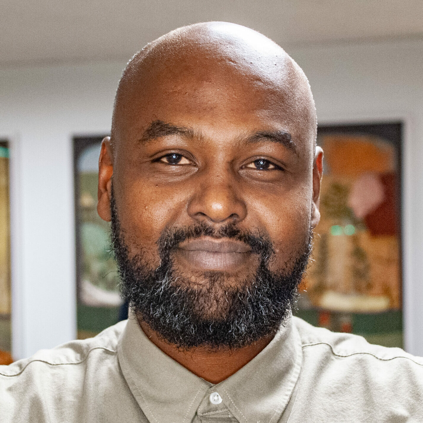 Hashim tittar in i kameran. Har har på sig en beige kofta.