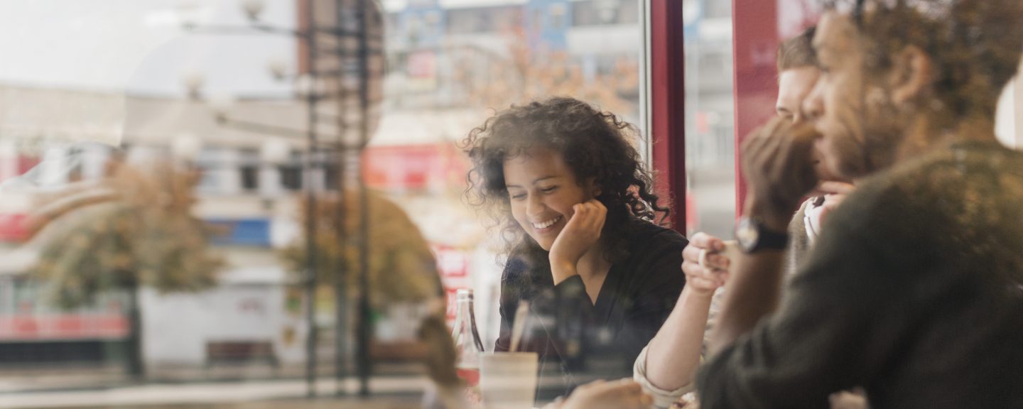 Ung glad kvinna sitter på kafé, genom fönster