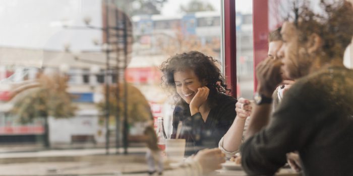 Ung glad kvinna sitter på kafé, genom fönster